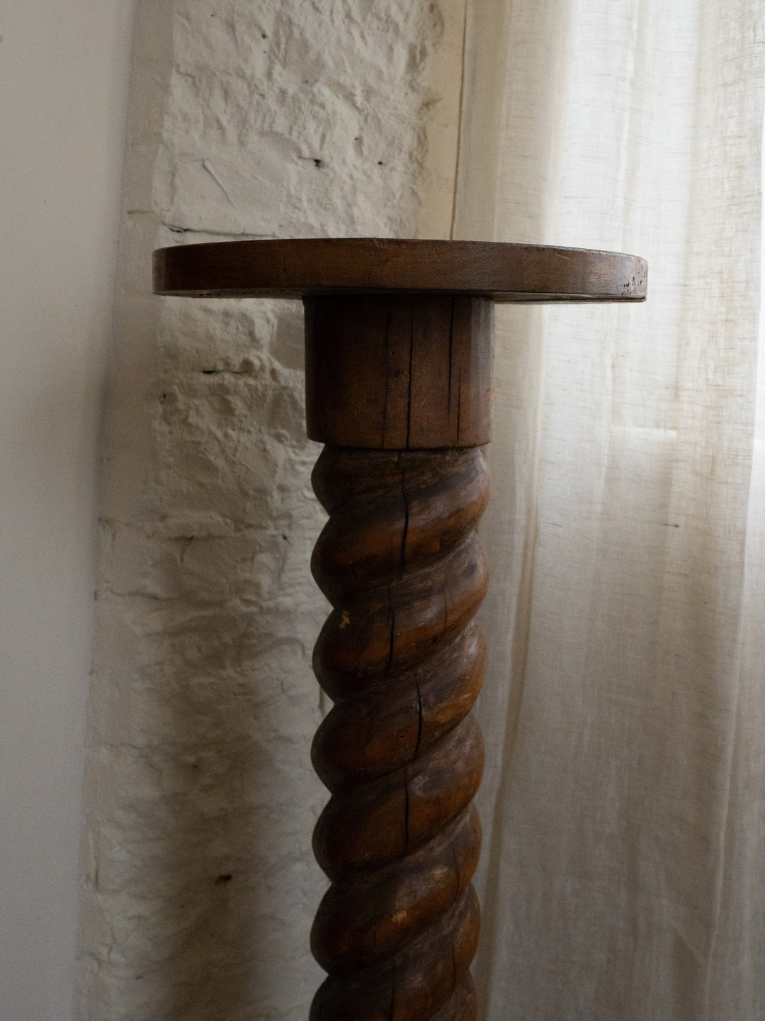 a wooden table with a twisted base is sitting in front of a brick wall