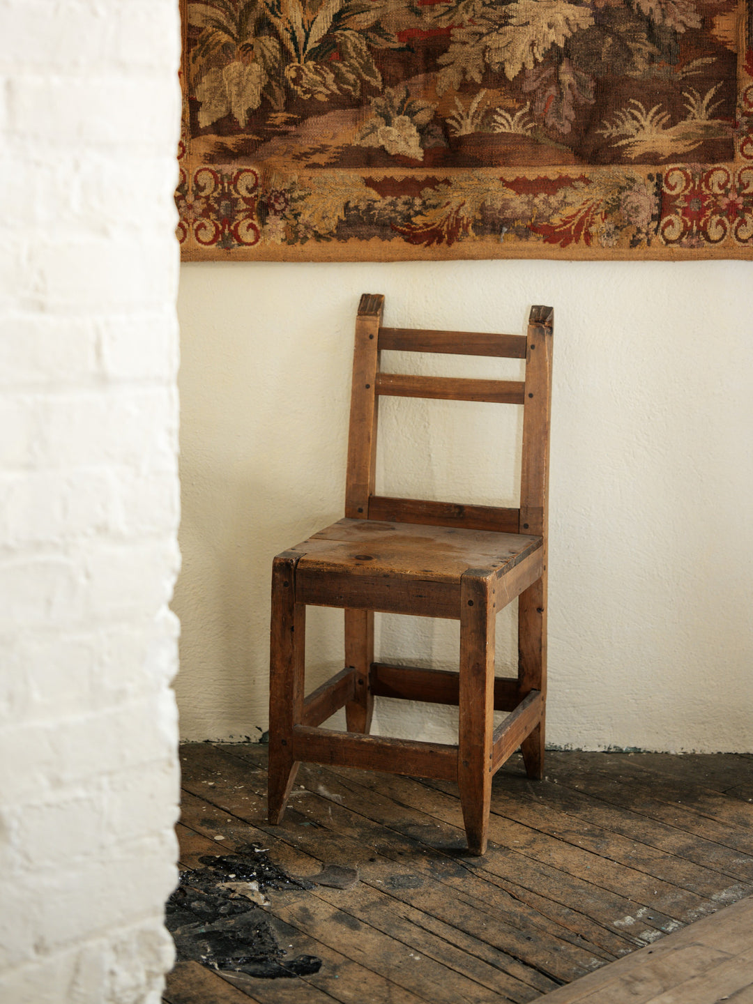 a wooden chair is sitting in a corner of a room next to a wall with a tapestry on it .