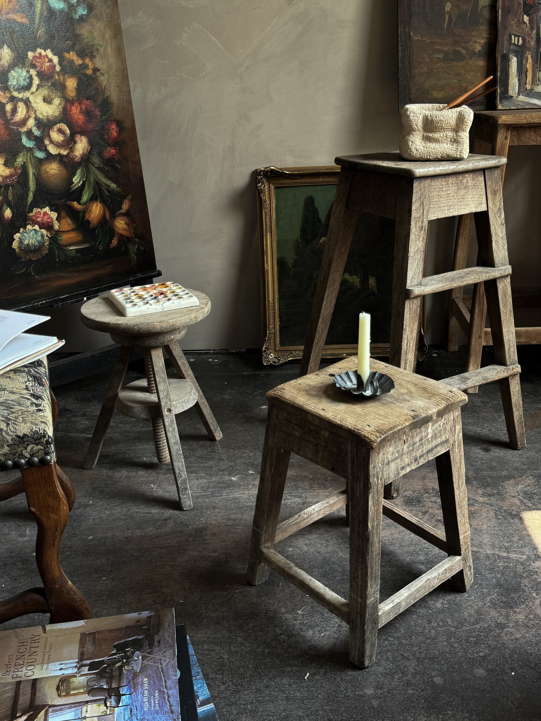 a candle sits on a wooden stool in front of a painting