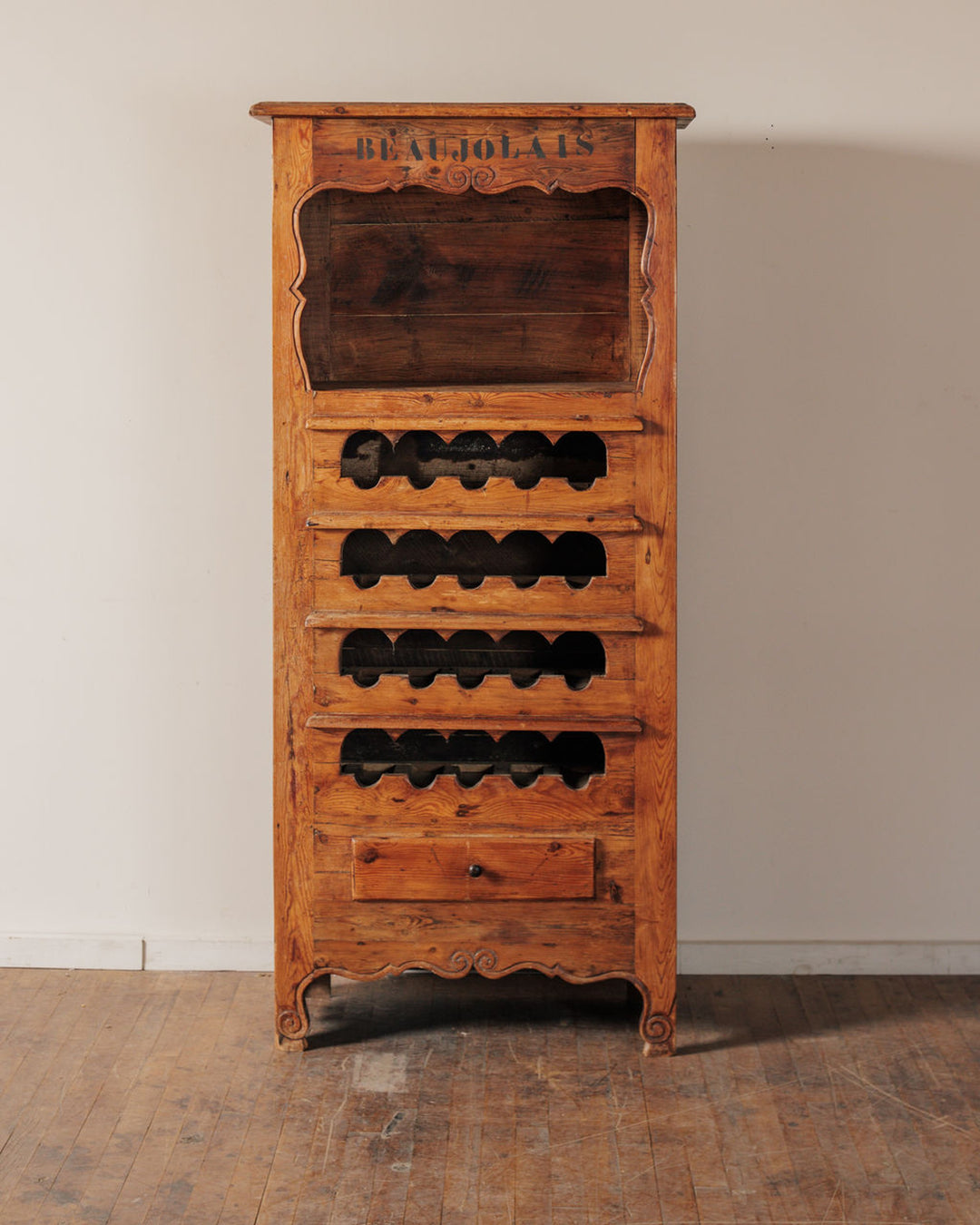 Rustic wooden wine cabinet with "BEAUJOLAIS" stenciled on top, featuring multiple bottle compartments and a small drawer.