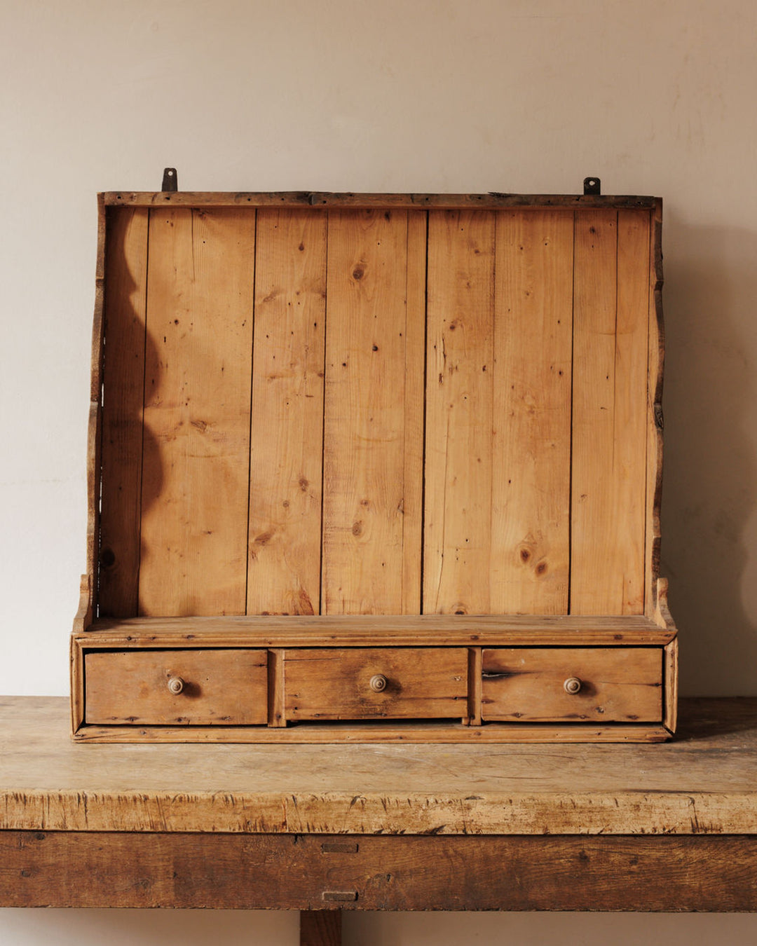 Antique wooden wall shelf with a slatted back and three small drawers.