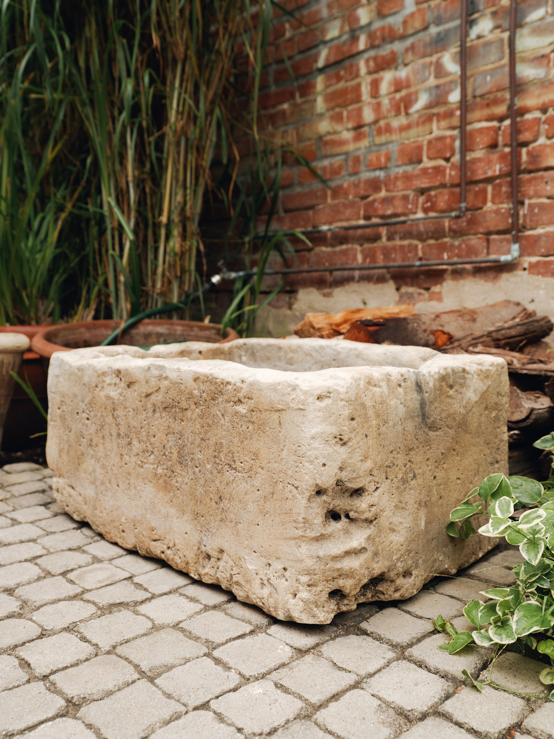 a large stone planter sits on a cobblestone patio in front of a brick wall
