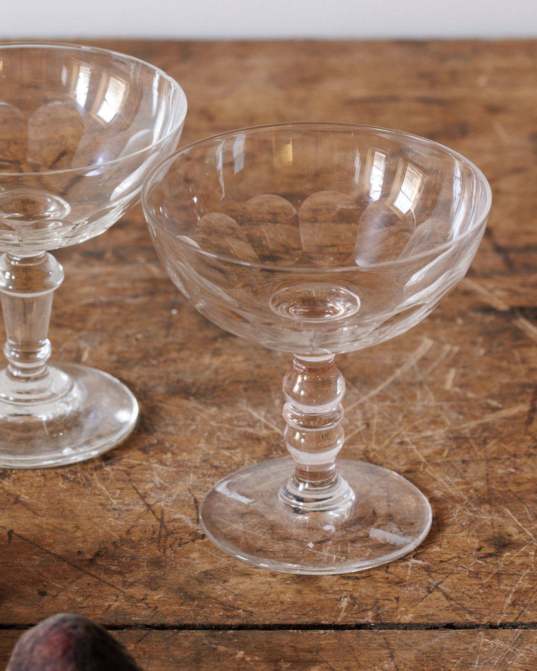 Two cut glass coupe glasses on a rustic wooden table.