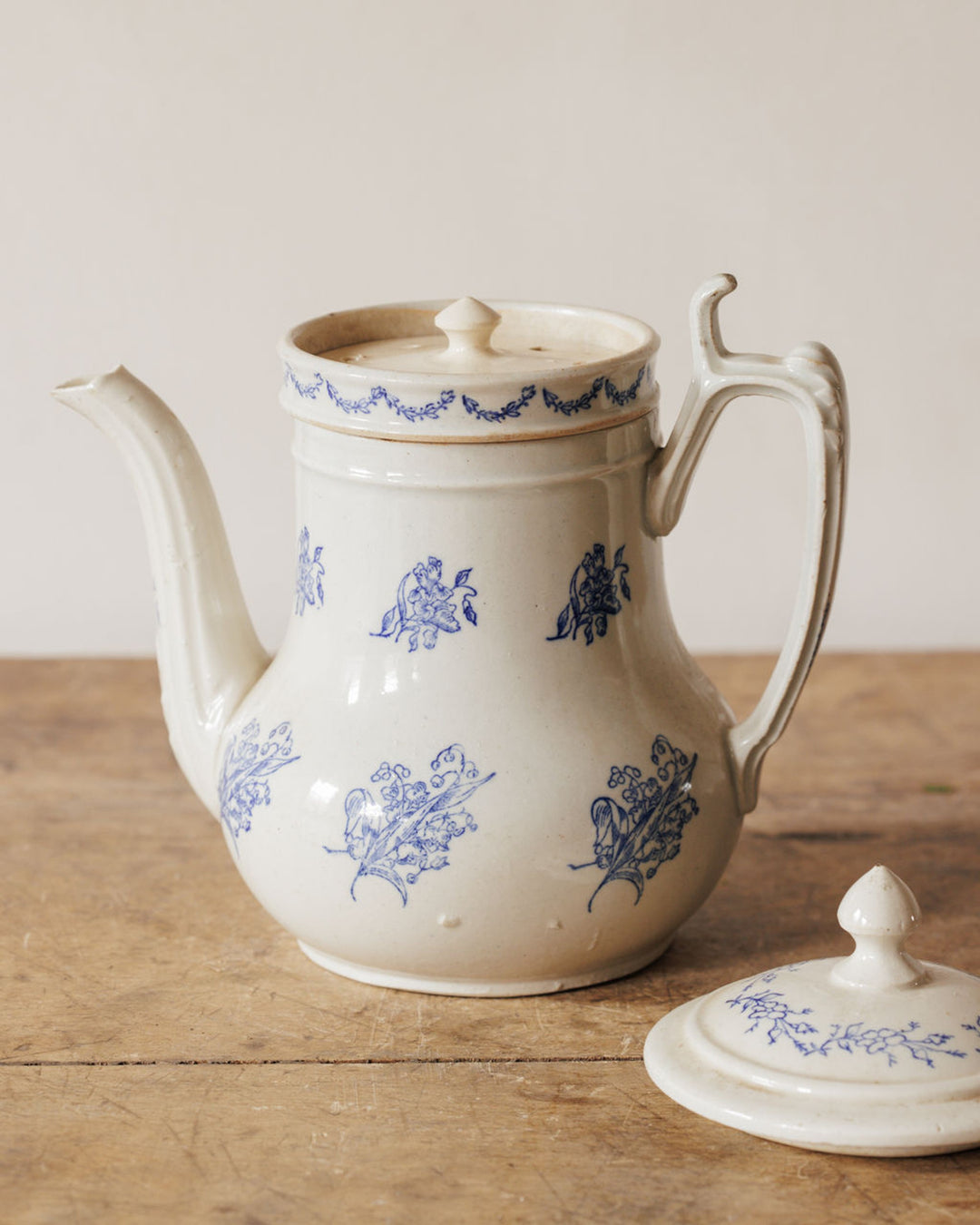 White ceramic pot with blue floral patterns and its detached lid, on a wooden table.