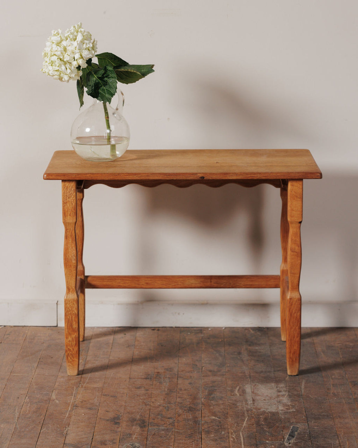 A light wood table with a glass pitcher of white hydrangeas.