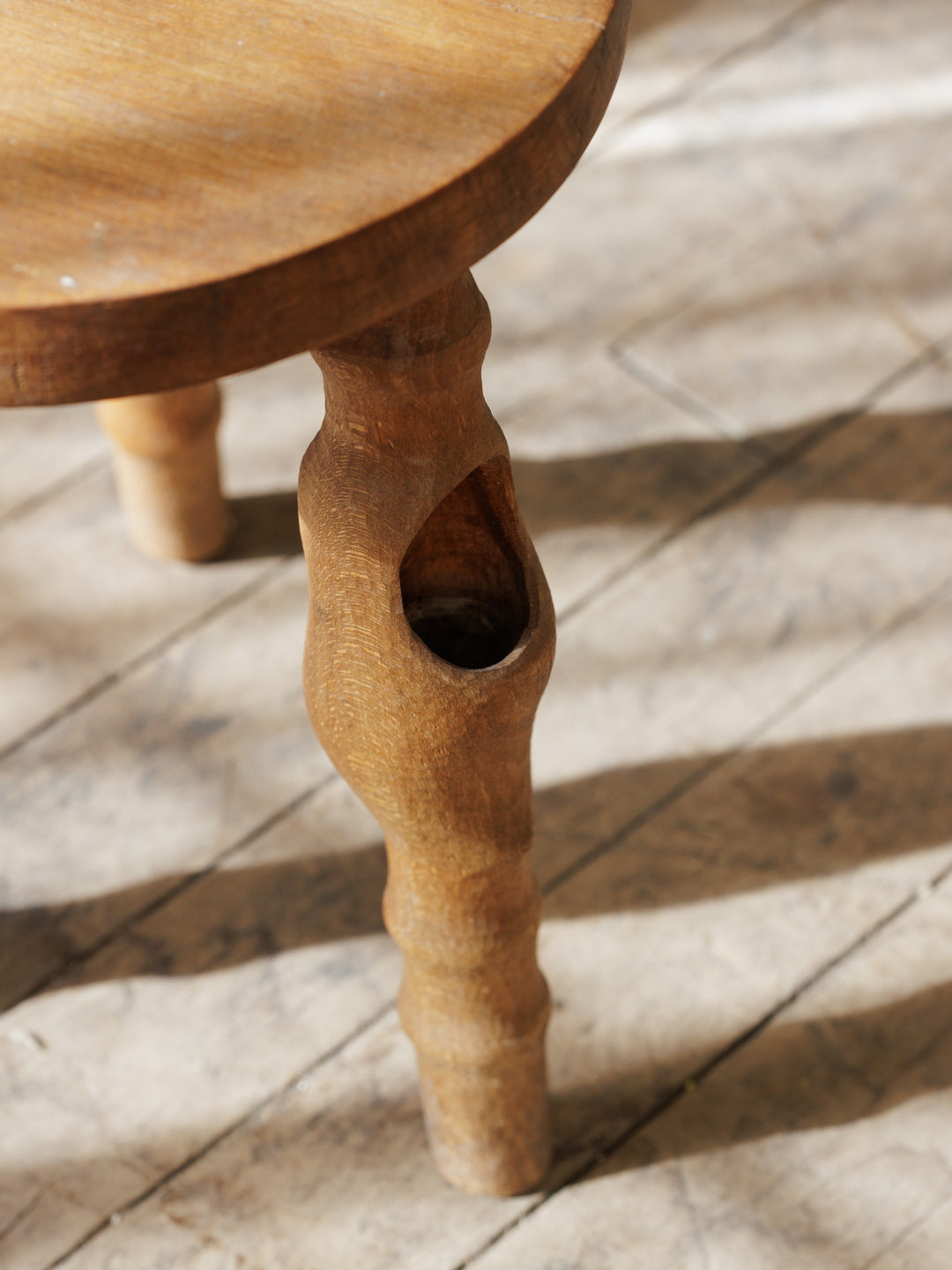 a wooden stool with a hole in the leg on a wooden floor .