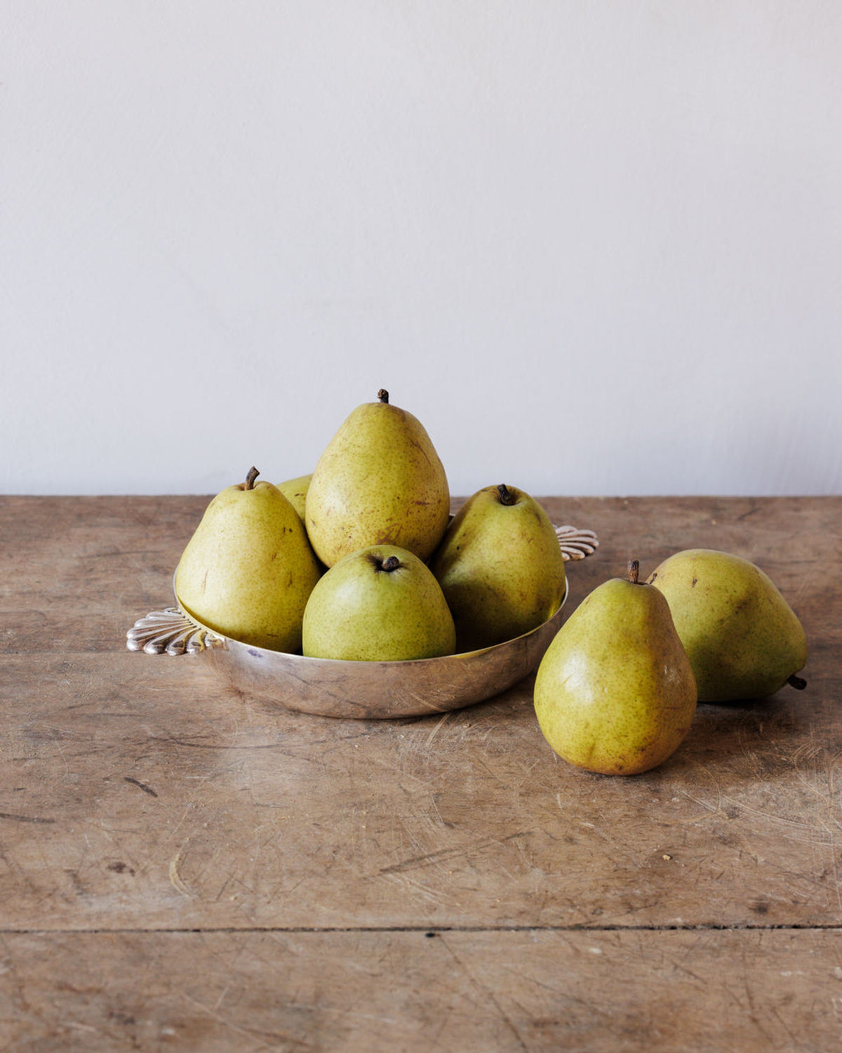 Yellow-green pears in a silver bowl and on a rustic wooden table.