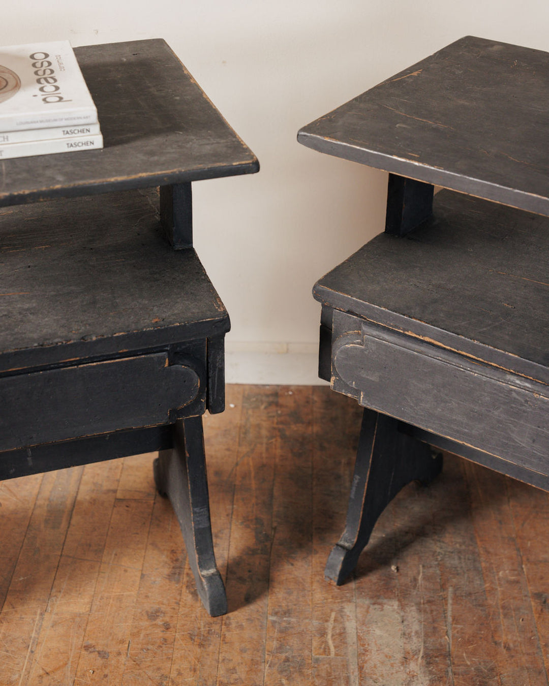 A pair of distressed black wooden side tables with open drawers on a rustic floor.