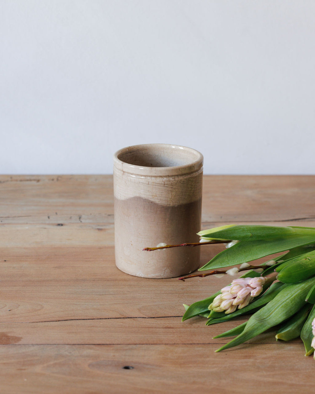 A two-toned ceramic pot with pink hyacinths and pussy willow branches on a wooden table.