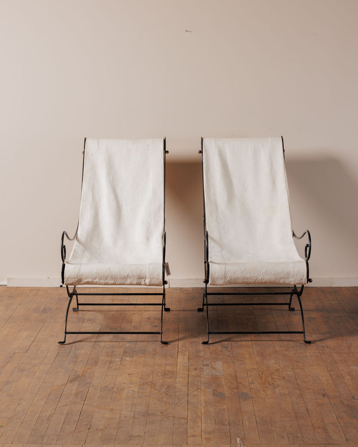 A pair of black wrought iron chairs with white canvas sling seats.