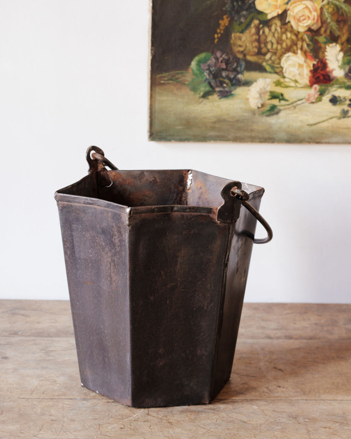 A dark, weathered hexagonal metal bucket with handles on a wooden surface.