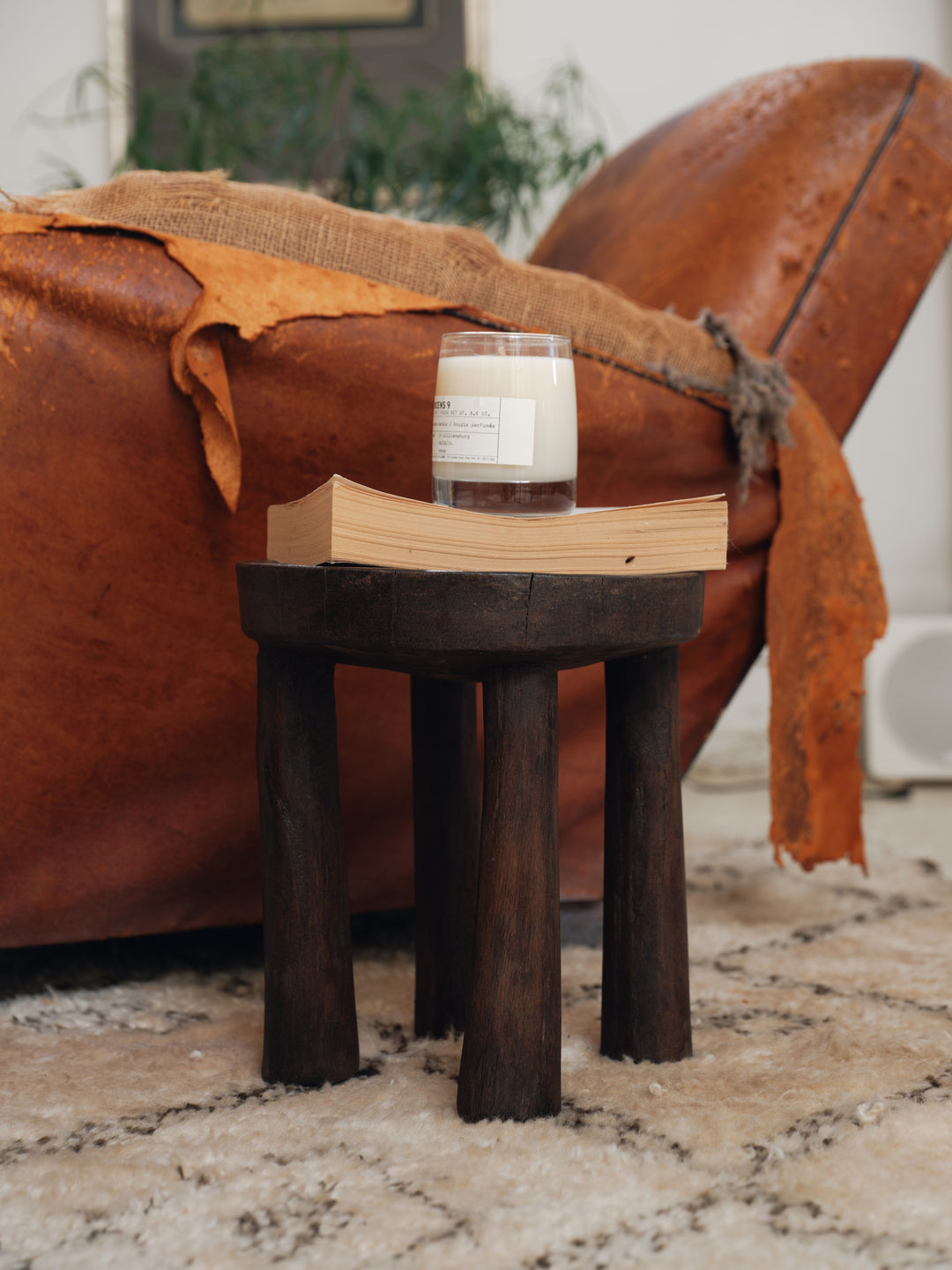 a wooden stool with a candle and a book on it in a living room .