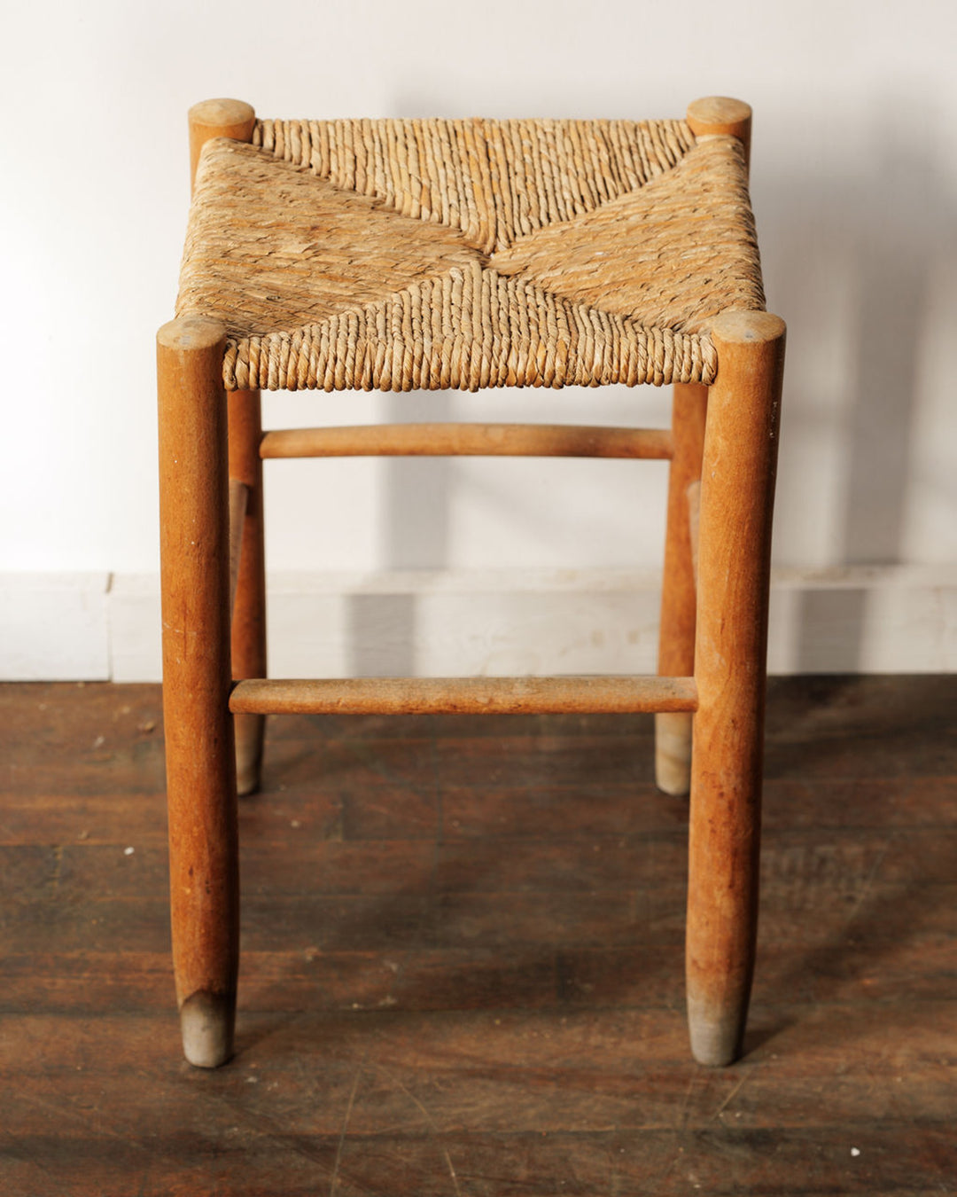 A wooden stool with a square woven rush seat.