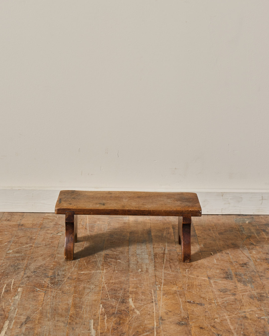A small, weathered wooden stool on a scratched wooden floor.
