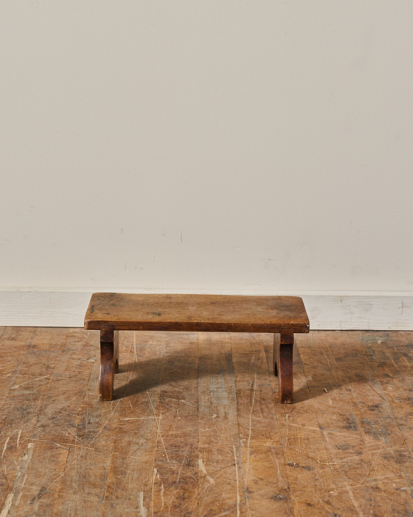A small, weathered wooden stool on a scratched wooden floor.
