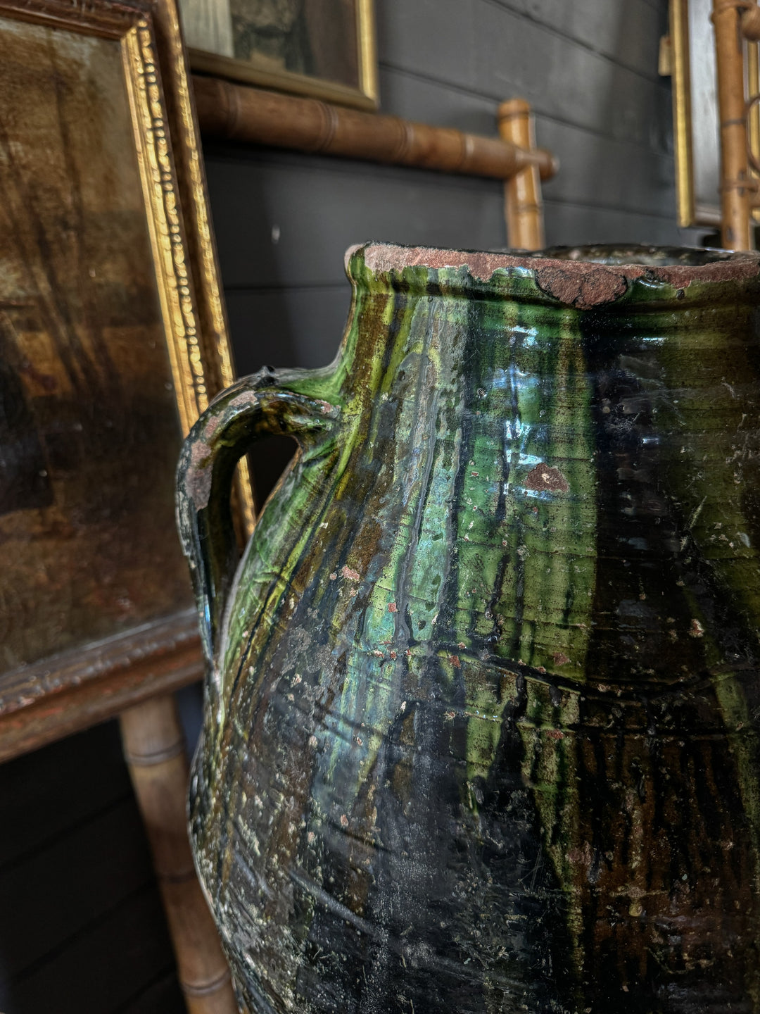 a green and black vase is sitting on a table next to a painting .