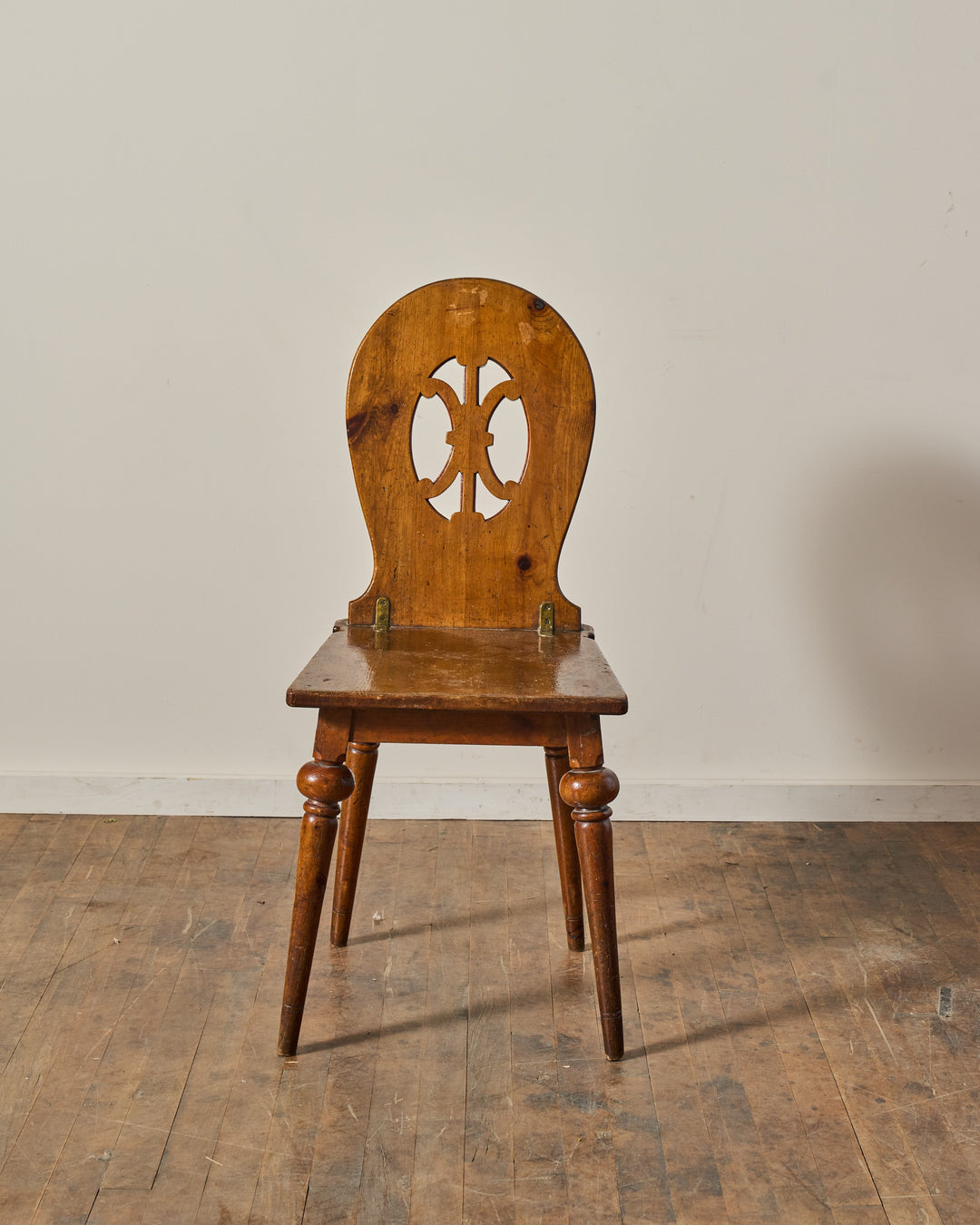 A vintage warm brown wooden chair with a hinged, decorative cutout backrest and turned legs.