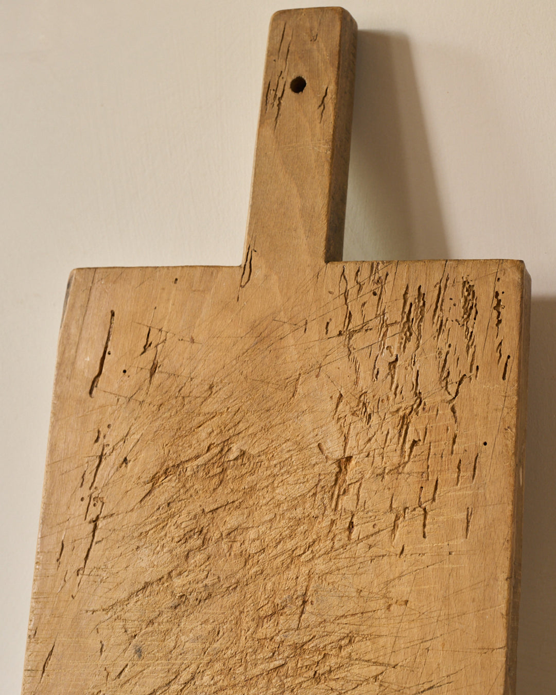 A heavily scratched wooden cutting board with a handle.