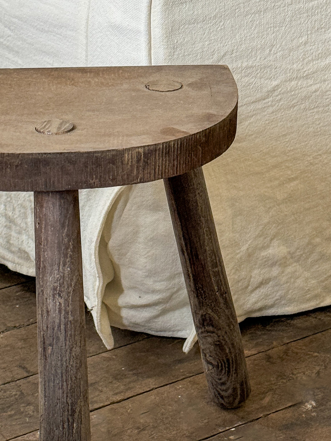 a wooden stool is sitting on a wooden floor next to a bed .
