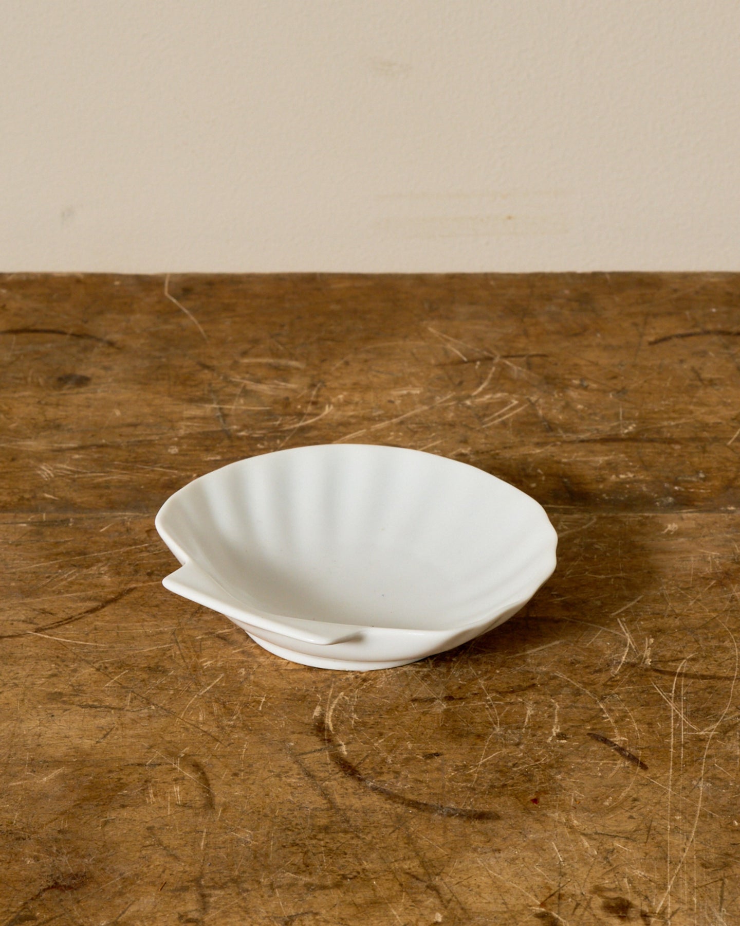 A white ceramic scallop shell dish sits on a rustic wooden surface.