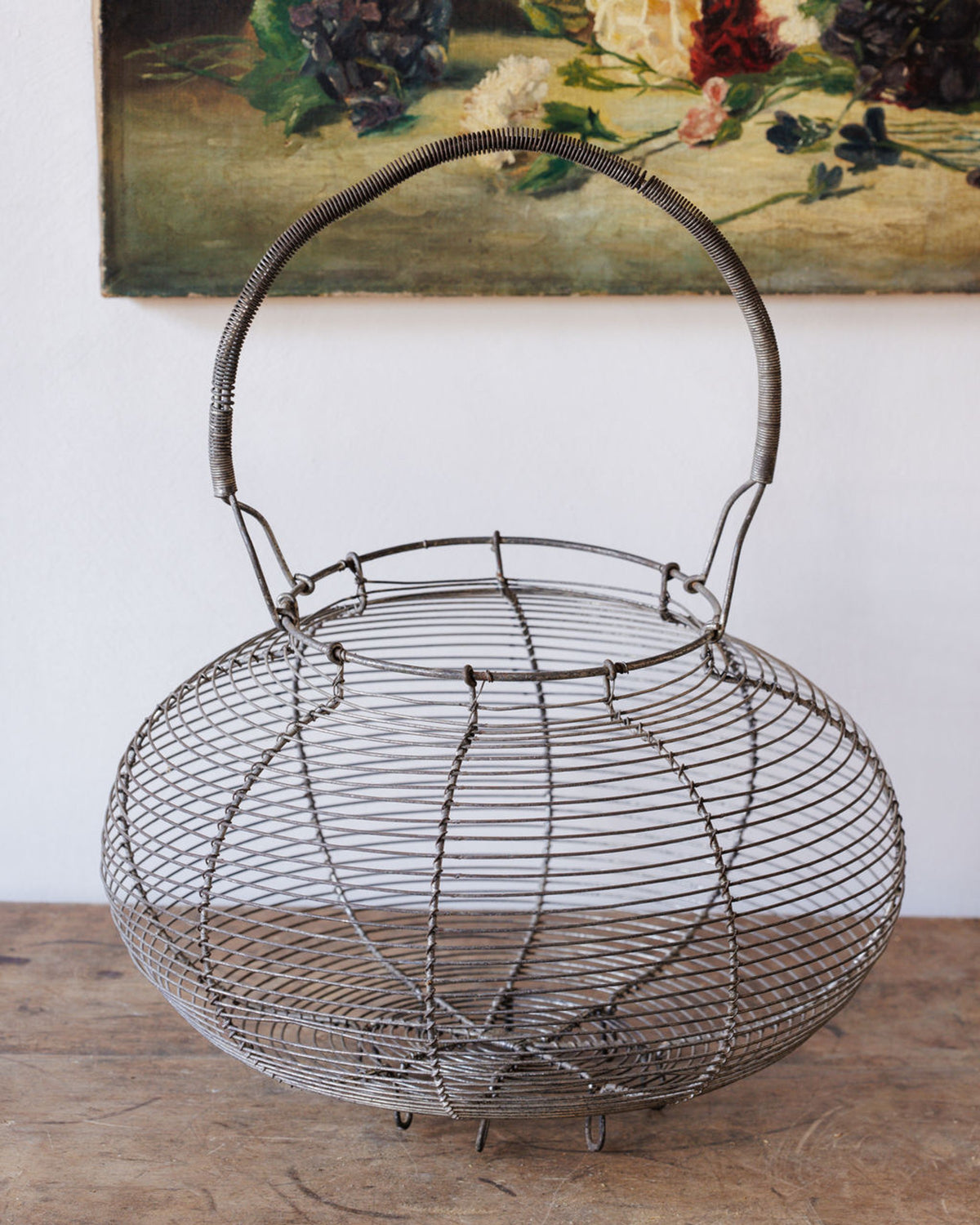 A vintage wire basket with a handle on a wooden surface.