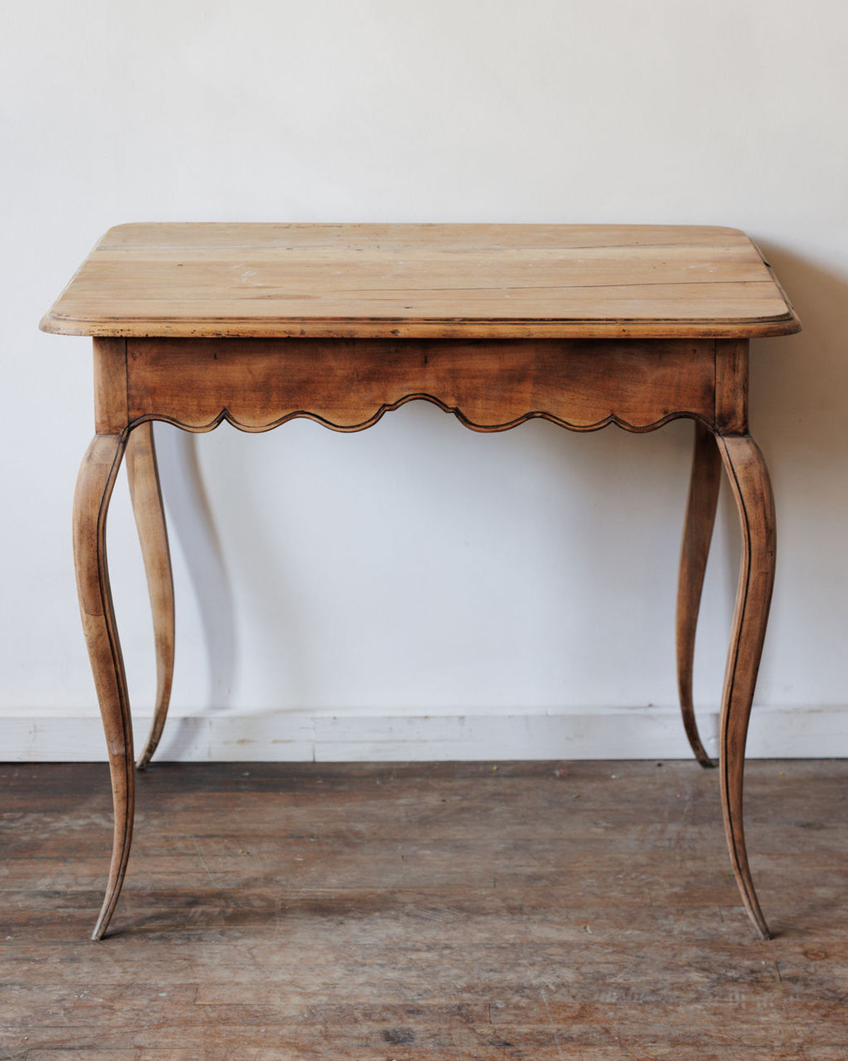 Antique wooden table with a scalloped apron and curved legs.