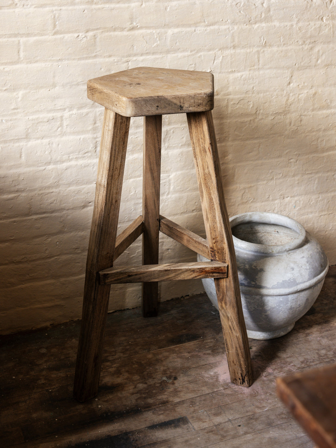 a wooden stool is sitting in front of a white brick wall with a willy guhl pot