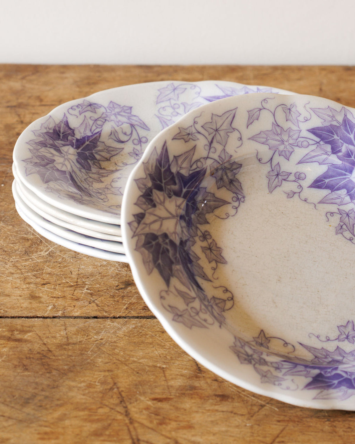 White scalloped plates with purple ivy designs stacked on a wooden surface.