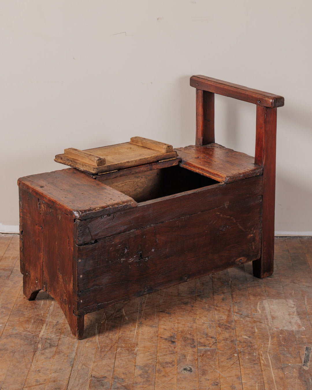 An antique wooden commode chair with an open lid revealing a compartment.