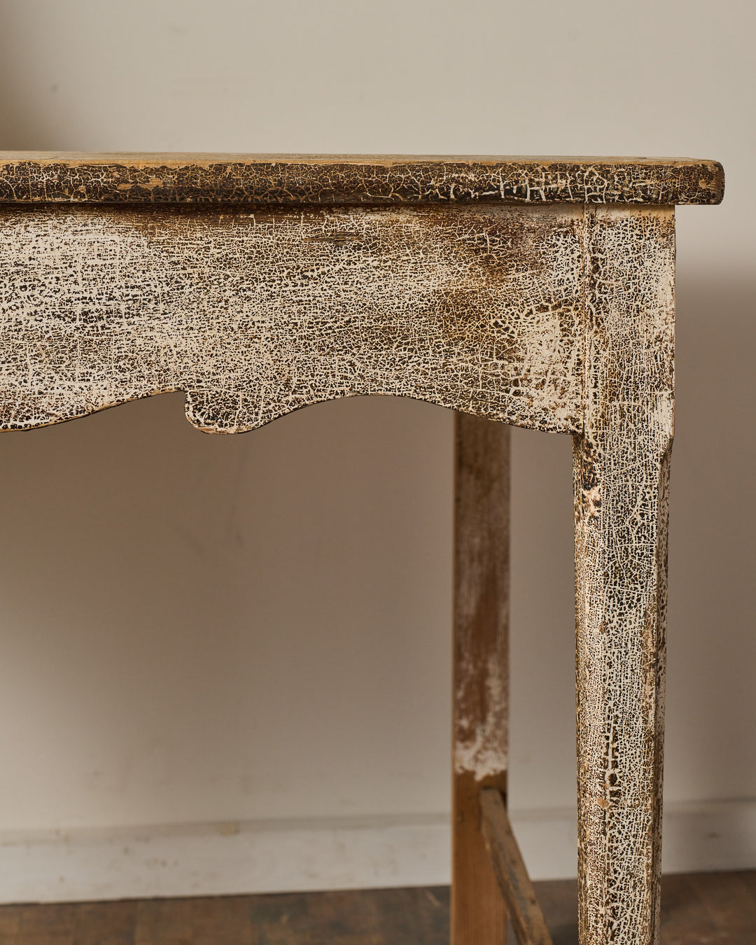 Close-up of a distressed wooden table with crackled white paint and a curved apron.