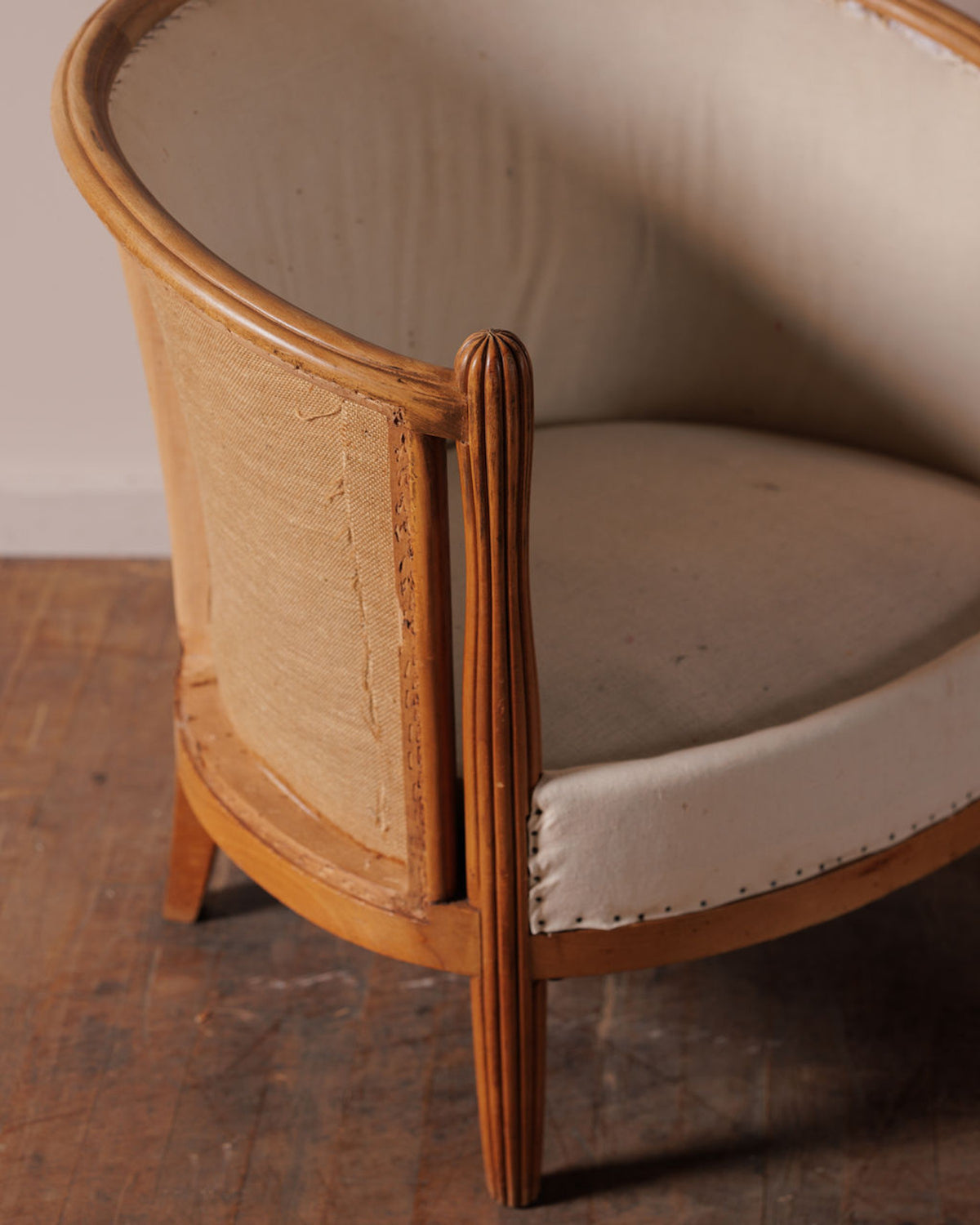 An antique wooden chair frame, partially upholstered in light fabric and raw burlap, with a fluted leg.