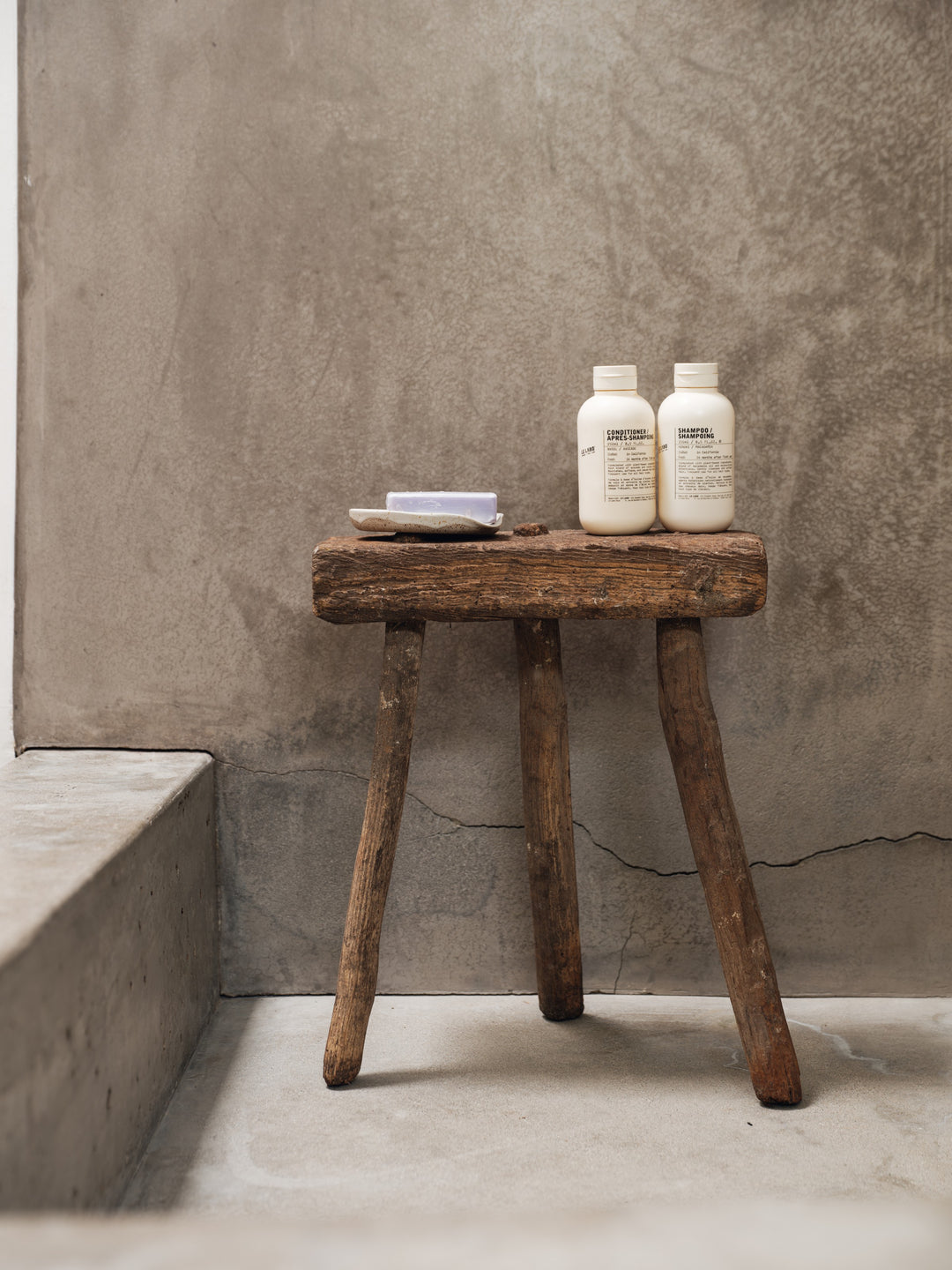 two bottles of shampoo are sitting on a wooden stool in a bathroom .