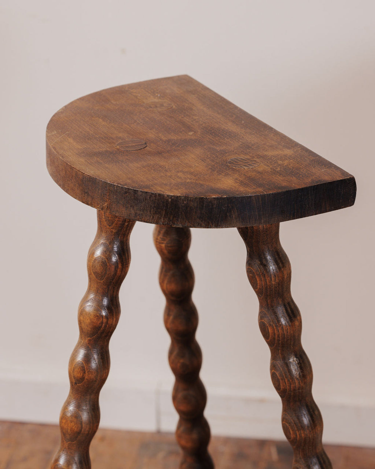 Dark brown wooden stool with a D-shaped seat and spiral-turned legs.
