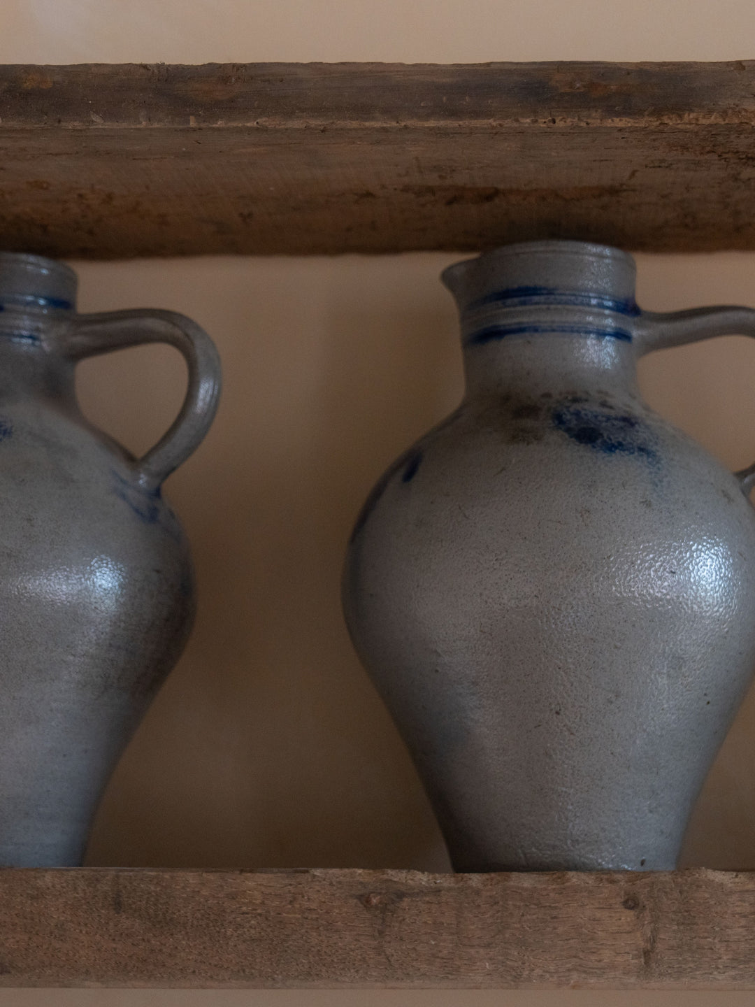 two gray vases with blue handles are sitting on a wooden shelf .