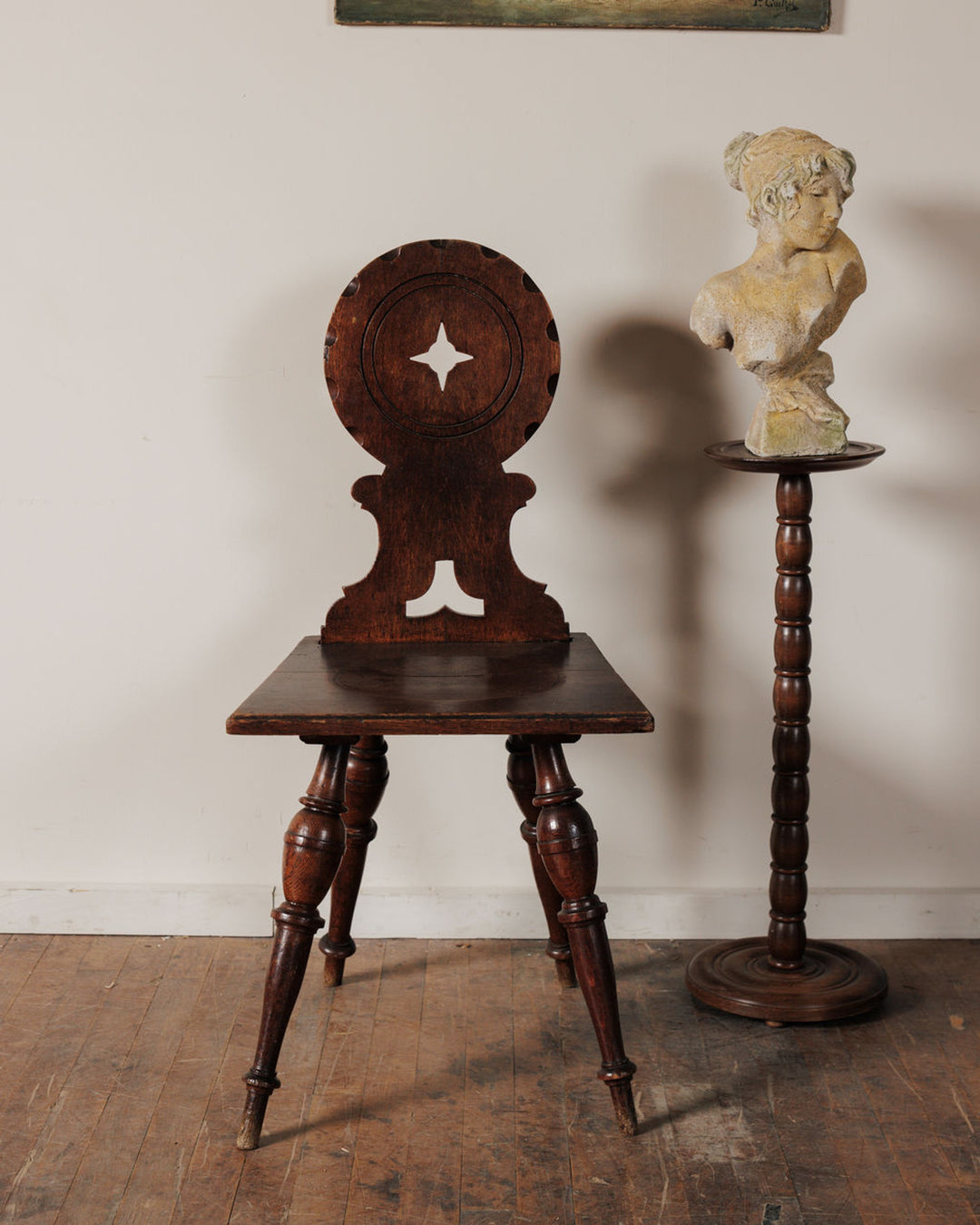 An antique dark wood chair with a carved star on its circular back, next to a pedestal holding a light-colored bust of a woman.