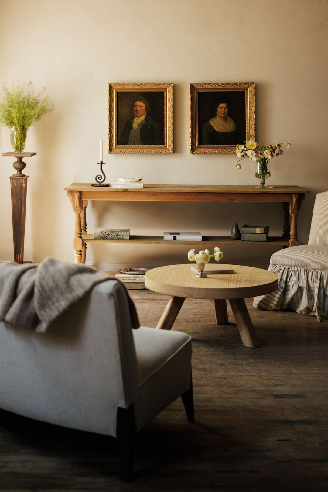 A cozy living room with two framed portraits over a wooden console table, a round coffee table, and two upholstered chairs.