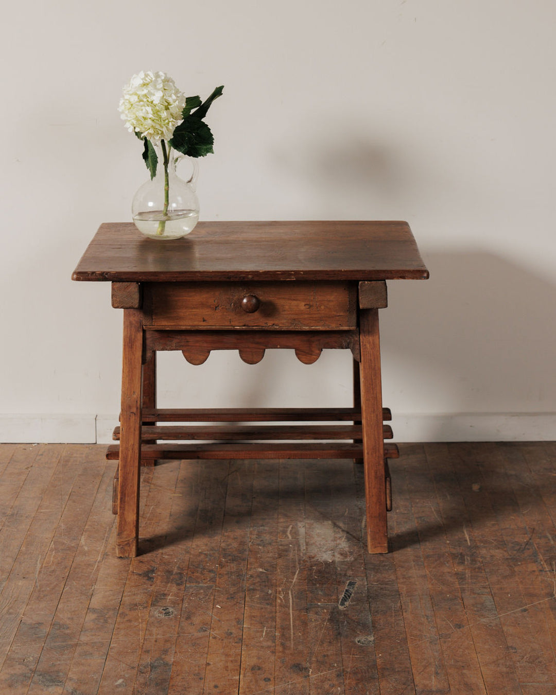 Rustic wooden side table with a drawer and a vase of white hydrangeas.