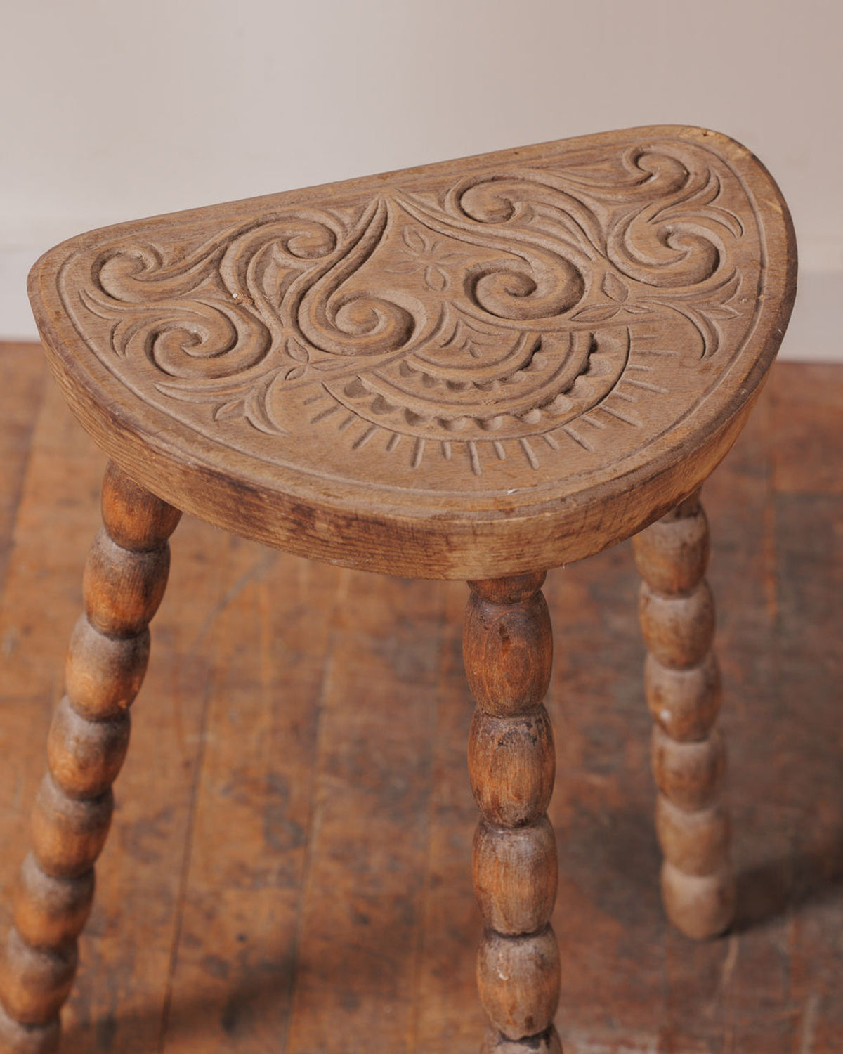 A carved wooden stool with a semicircular, ornate top and turned bobbin legs.