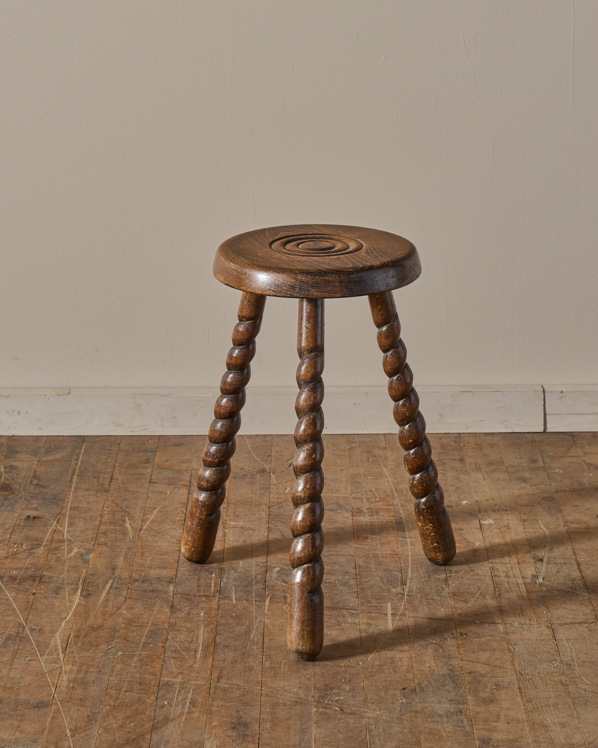 A dark wooden stool with a round seat featuring a carved spiral design and three twisted legs.