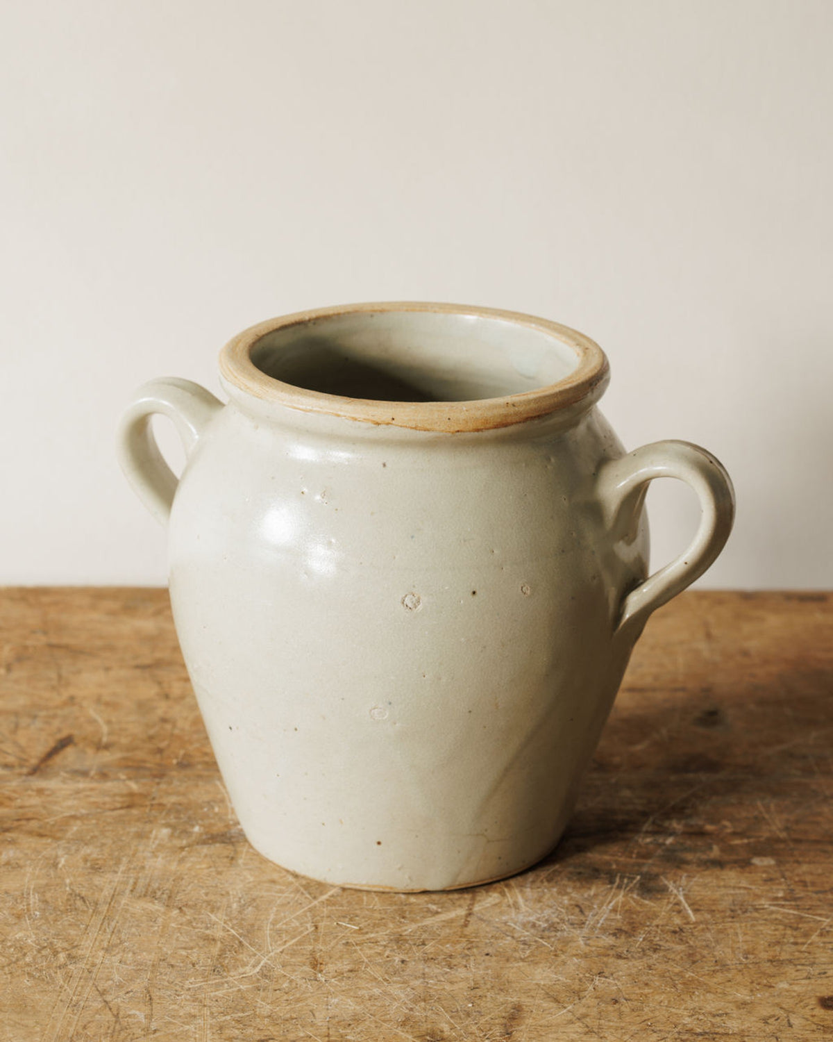 Rustic light-colored stoneware pot with two handles on a wooden table.