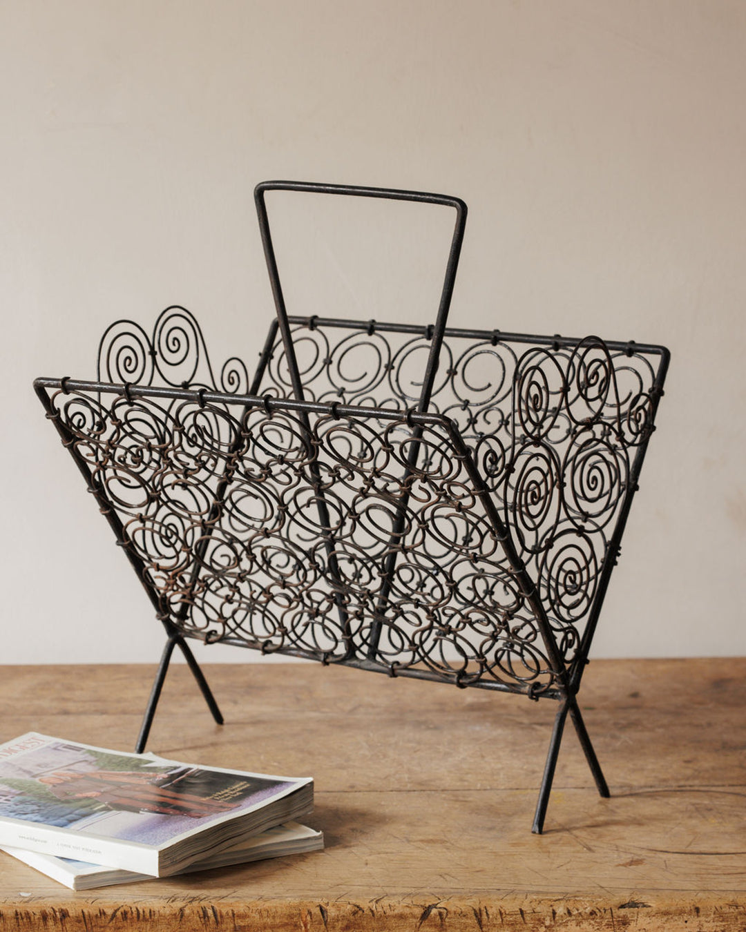 Dark metal scrollwork magazine rack on a wooden table.