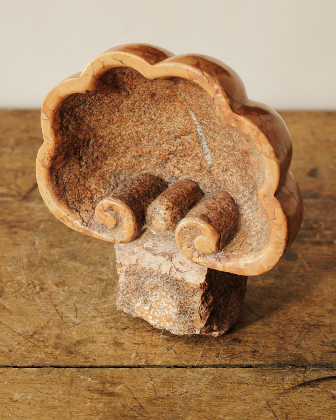 Scalloped, reddish-brown stone sculpture with three internal scroll forms on a wooden surface.