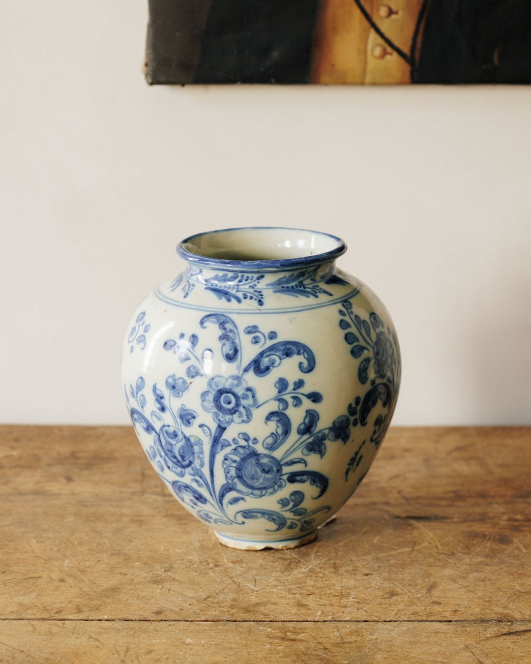 A rounded white vase with intricate blue floral patterns sits on a wooden table.