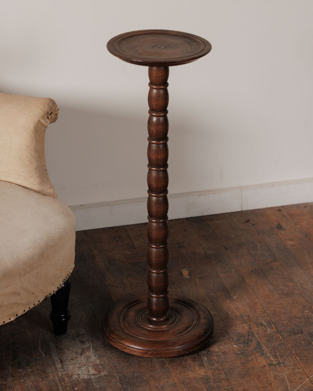 A tall, dark wood bobbin-turned pedestal stand with a round top and base.