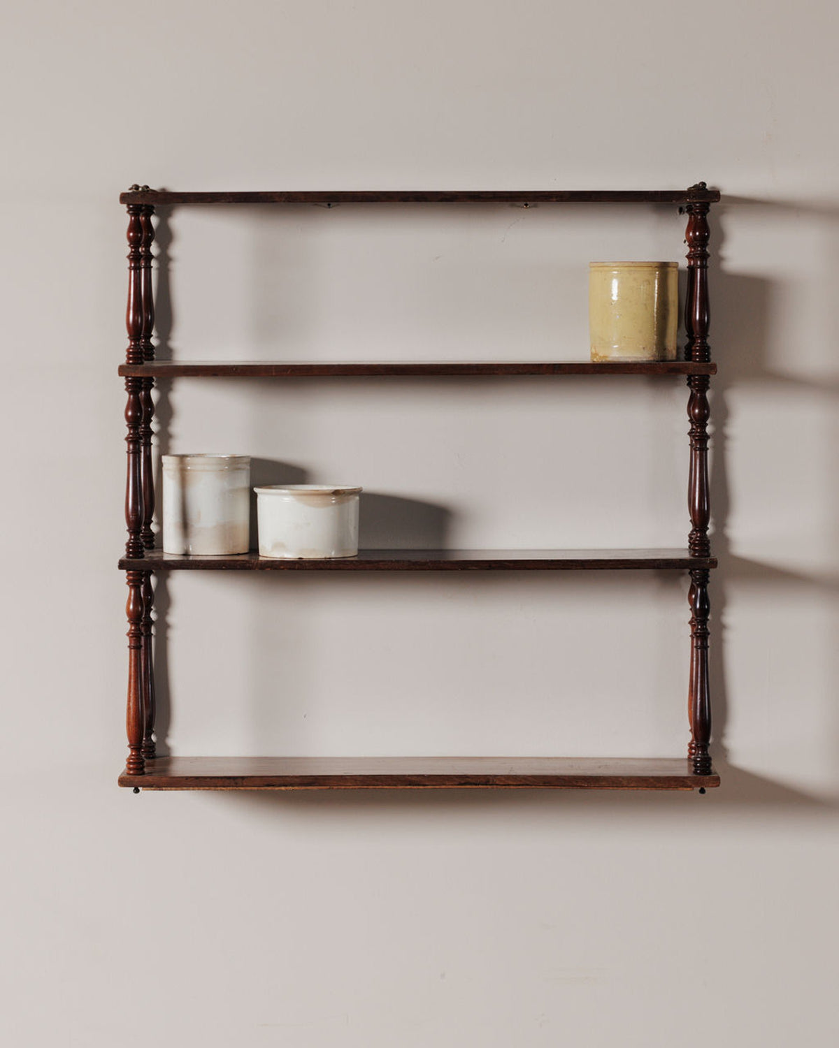 Four-tier wooden wall shelf with turned supports, holding three ceramic pots.