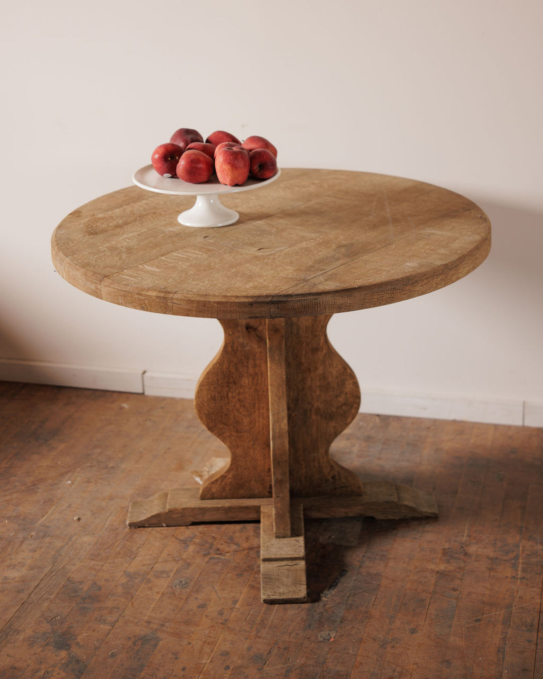Rustic round wooden table with red apples on a white stand.
