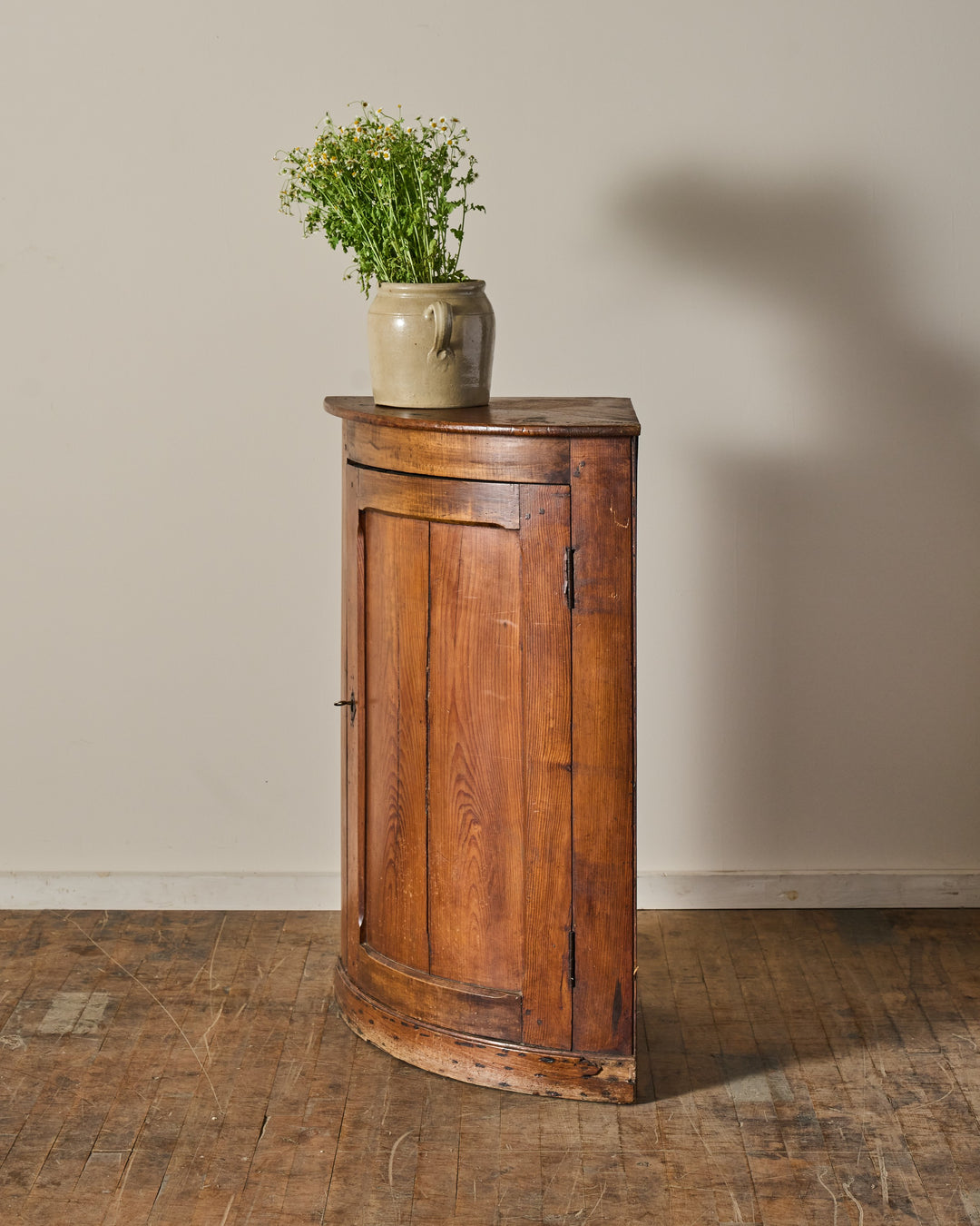 Antique wooden corner cabinet with a vase of flowers on top.