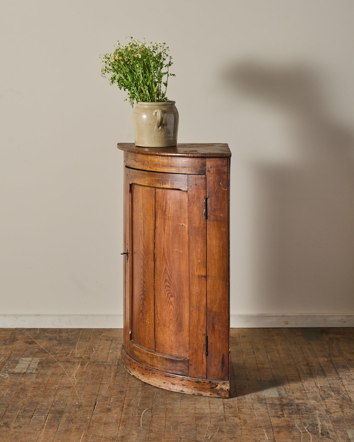 Antique wooden corner cabinet with a vase of flowers on top.