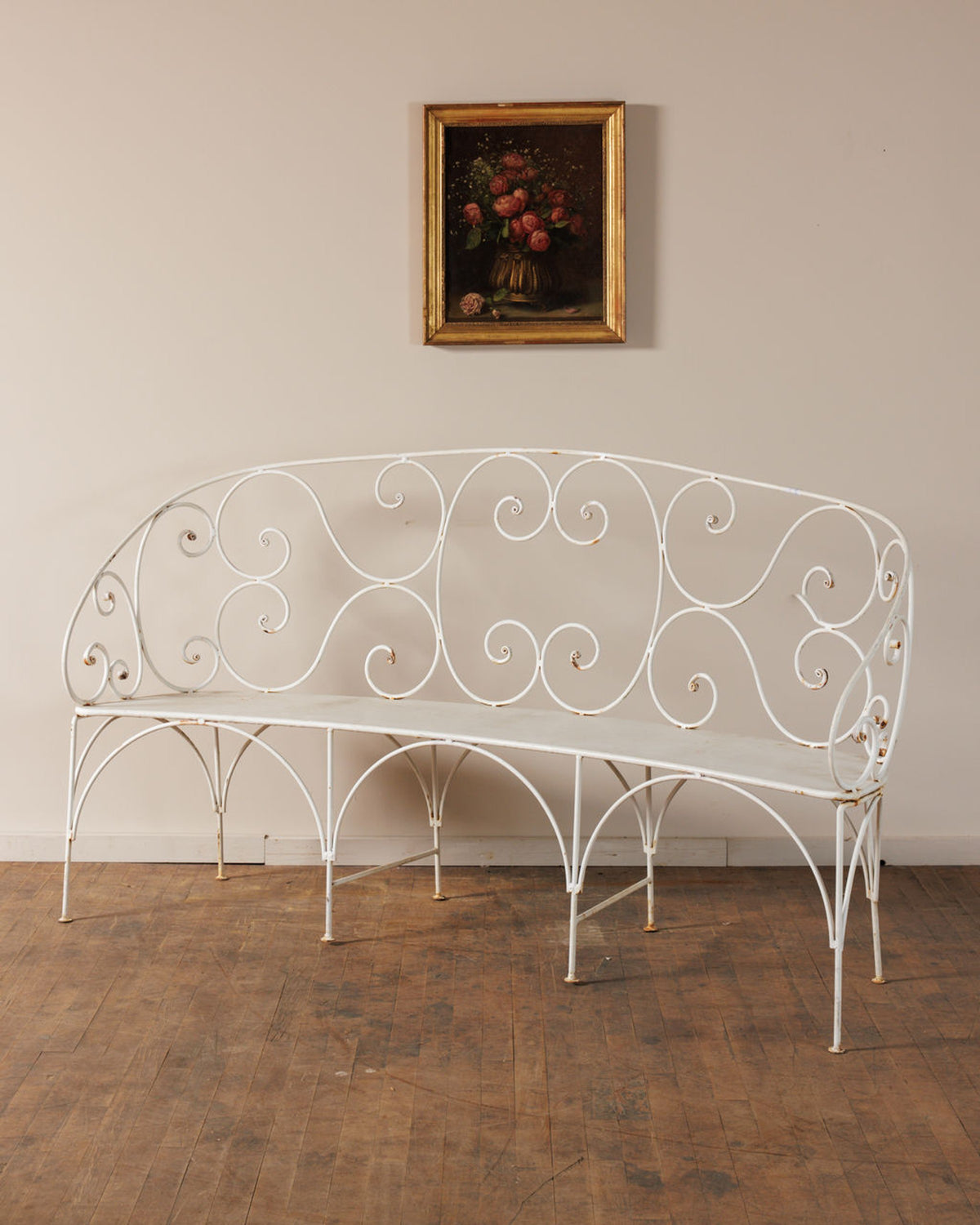 Ornate white wrought iron bench below a framed floral painting.