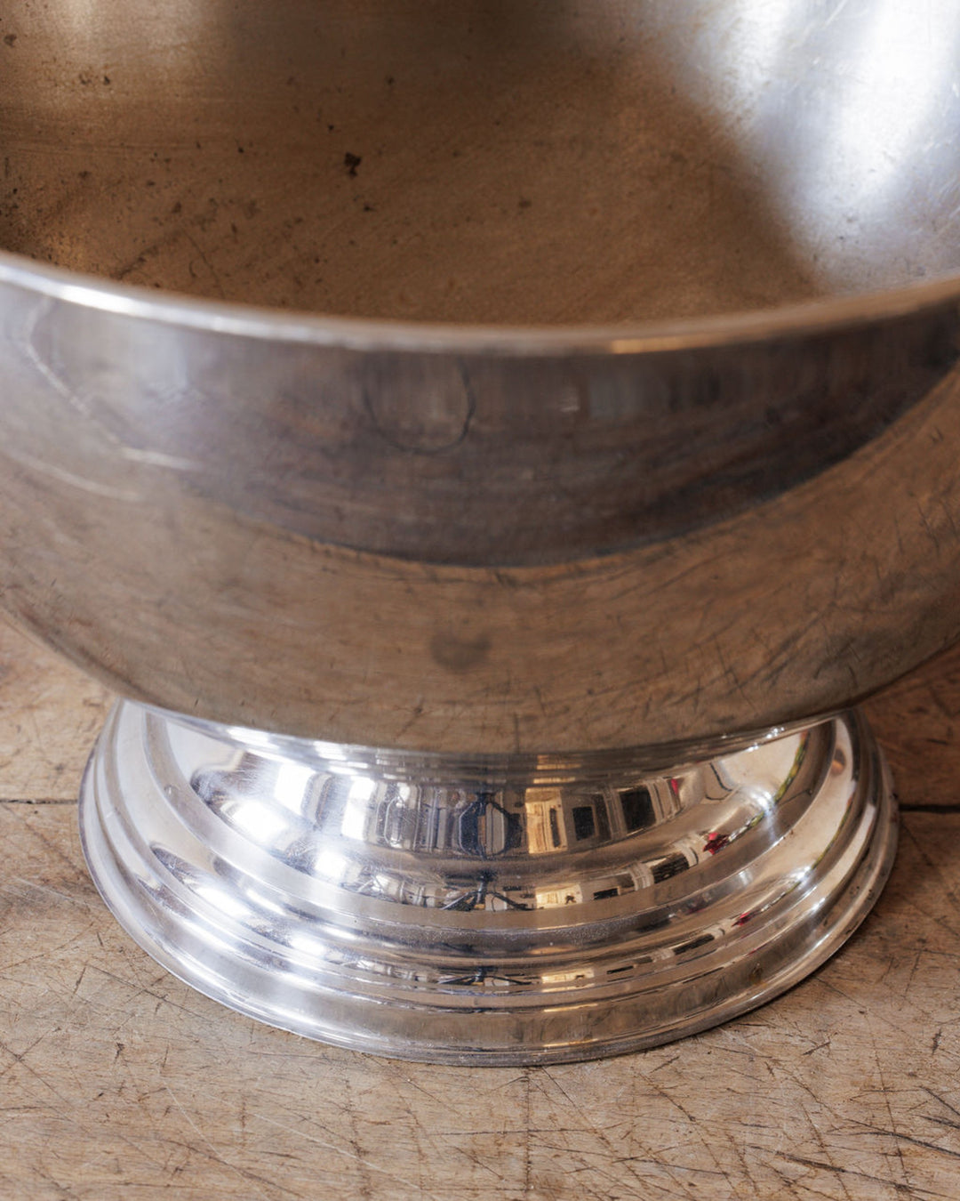 A tarnished metal bowl with a polished, reflective base on a rustic wooden surface.
